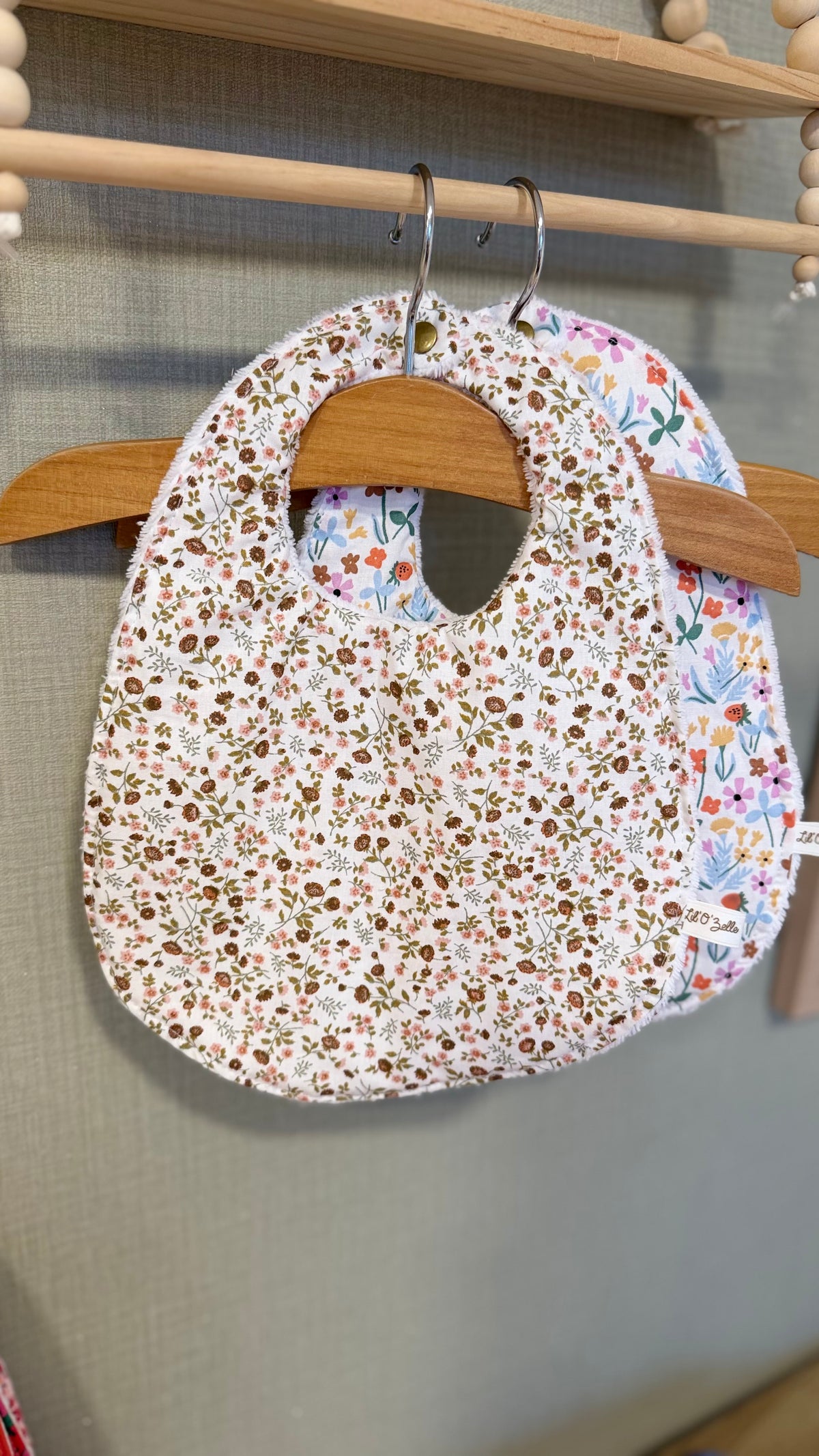 Bavoir bébé Lunelle à petites fleurs marron et ocre sur fond écru, suspendu à un cintre en bois