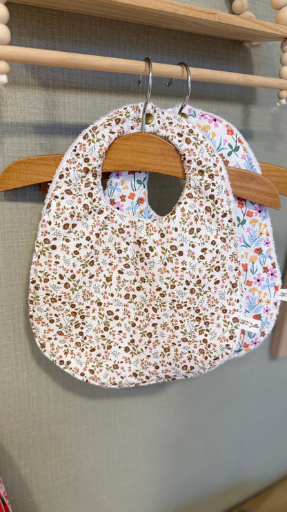 Bavoir bébé Lunelle à petites fleurs marron et ocre sur fond écru, suspendu à un cintre en bois
