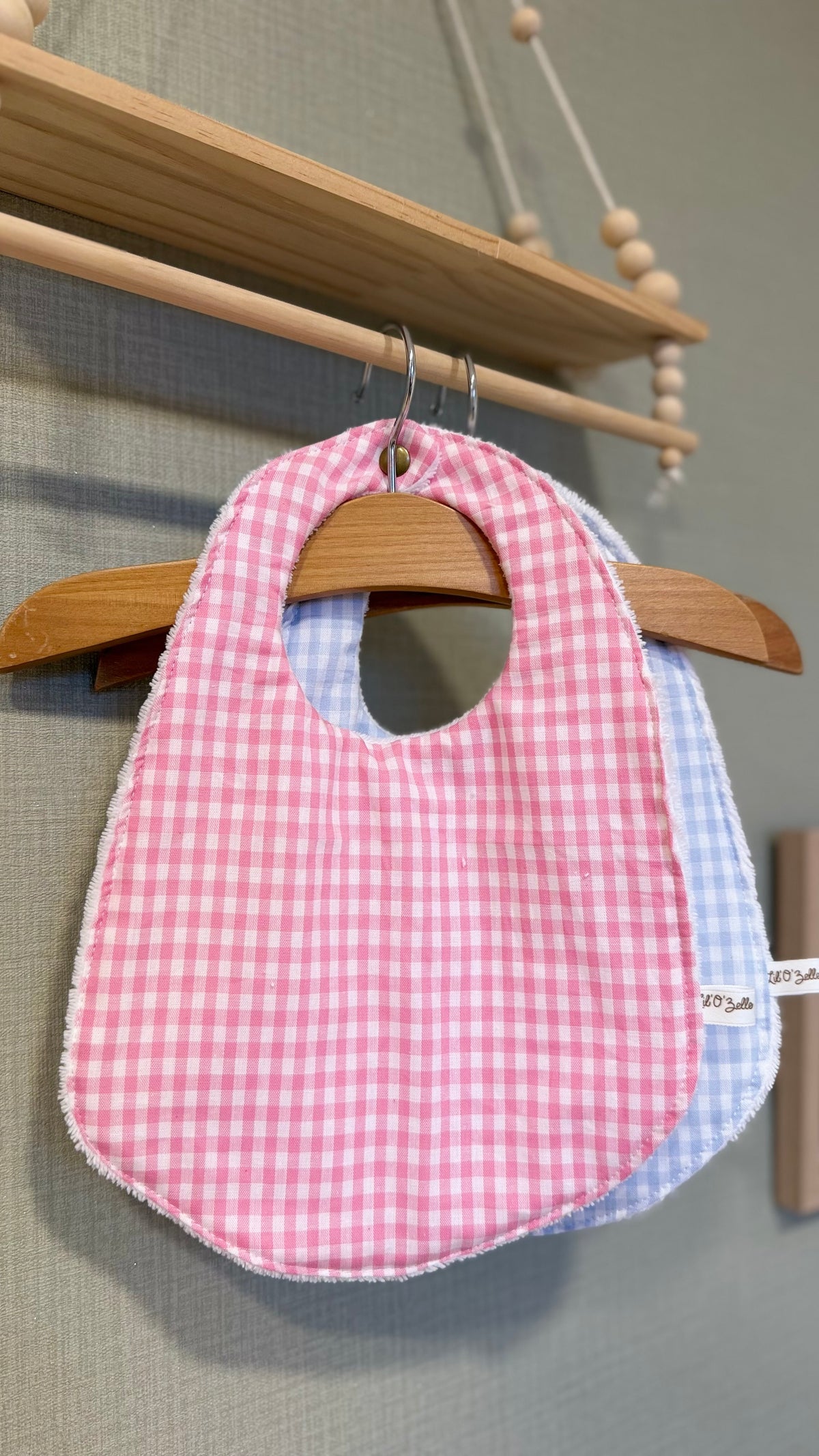 Bavoir bébé Lunelle en vichy rose, vue de face sur un cintre en bois