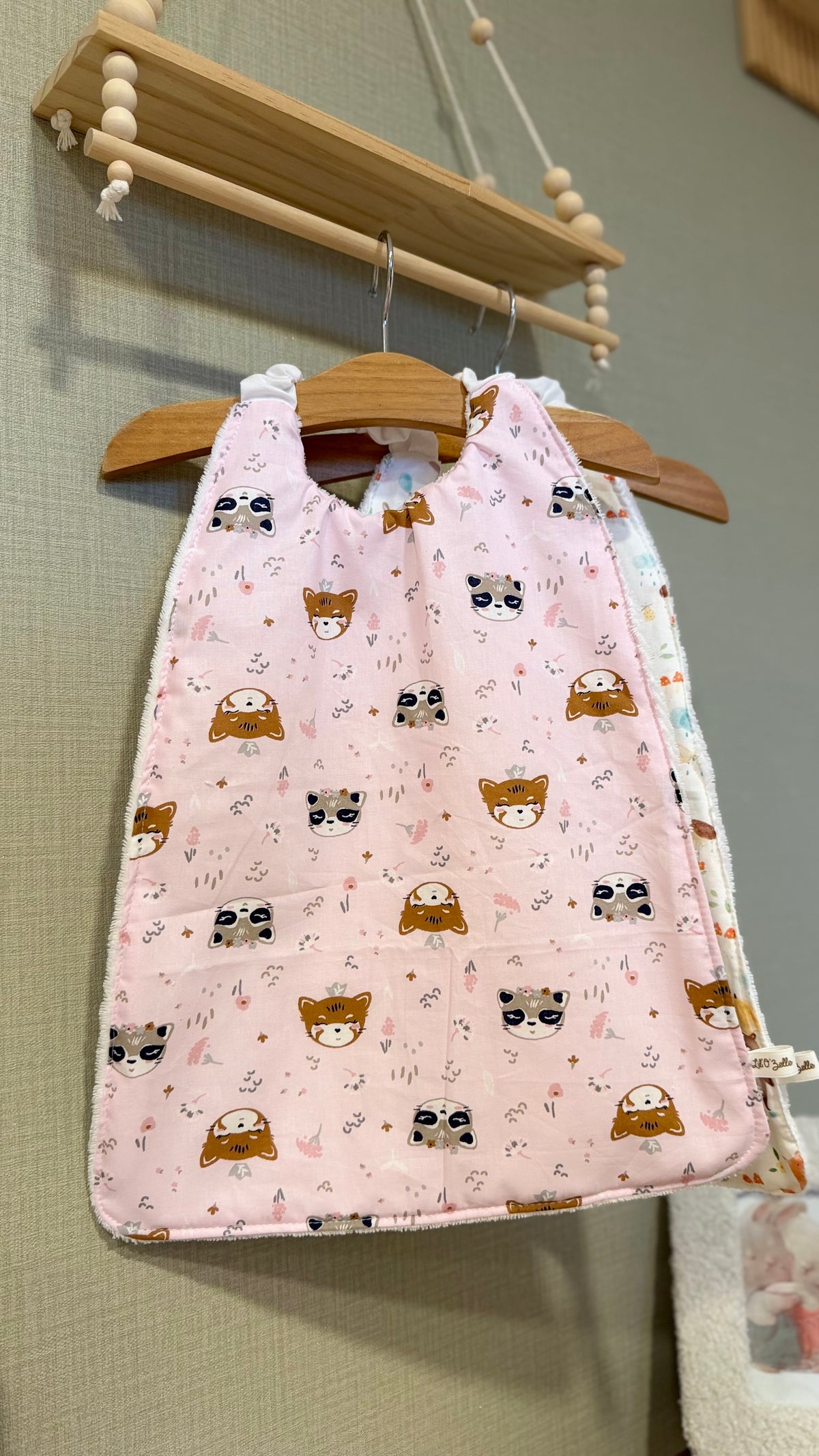 Grand bavoir maternelle Zouzou motif têtes de ratons laveurs et renards sur fond rose pâle