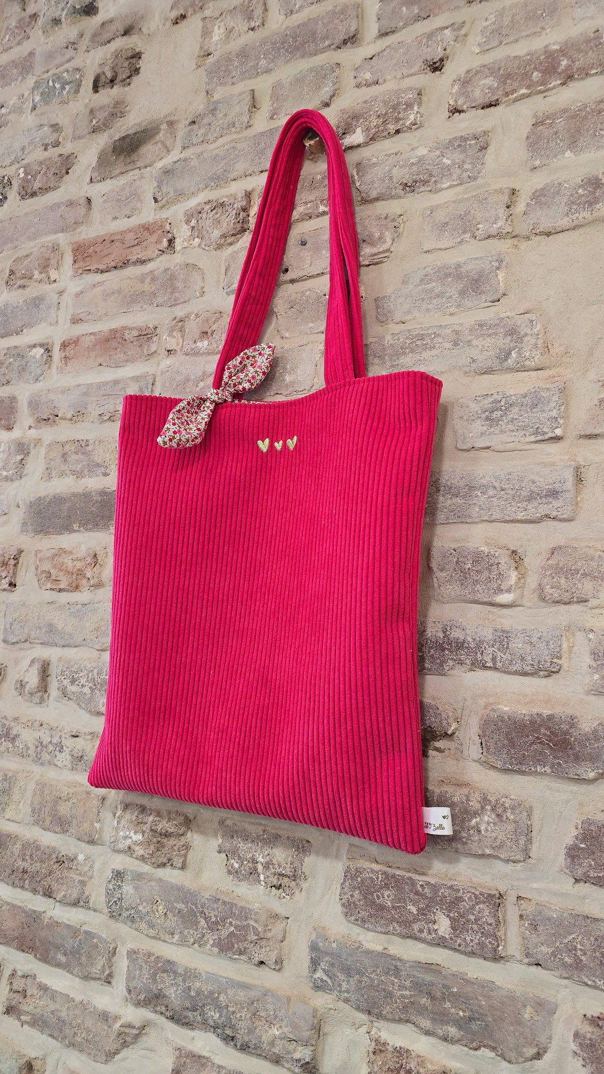 Totebag velours Soléa personnalisé, velours framboise suspendu contre un mur de briques